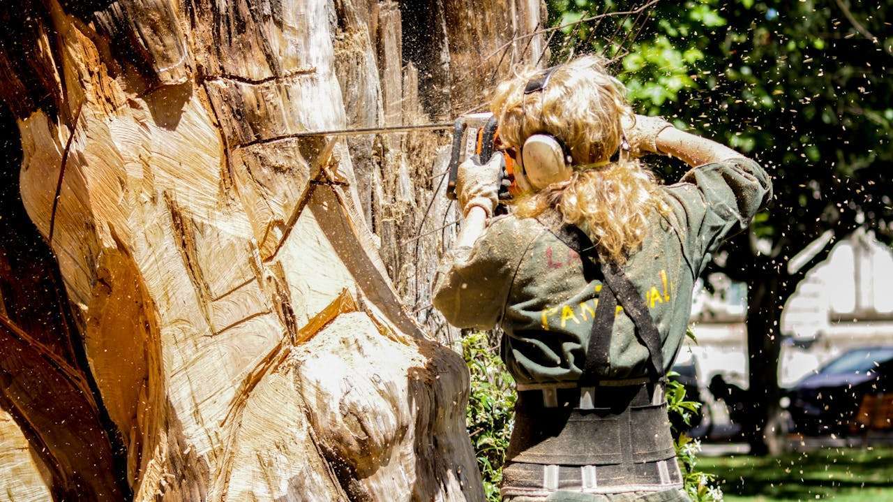 A skilled woman arborist cuts a large tree with a chainsaw outdoors, showcasing expertise in tree care.